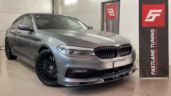 Ein grauer Alpina D5 S steht neben dem Banner der Fastlane Tuning Schweiz GmbH. An der Front des Autos liegt Schnee.