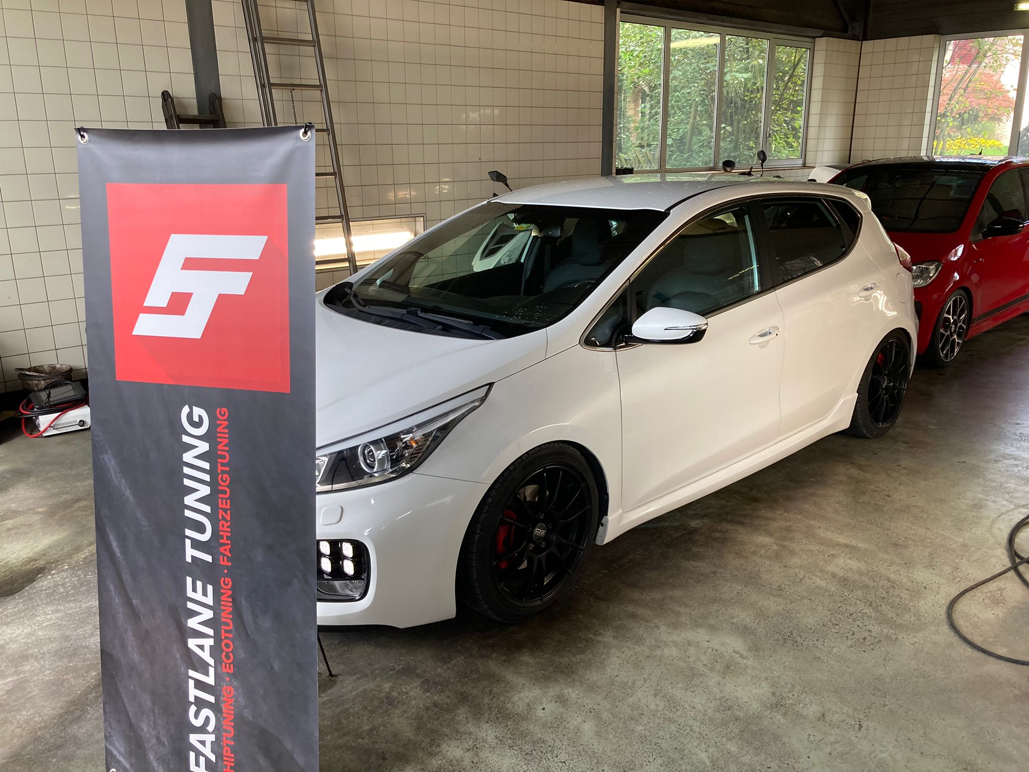 Ein weisser Kia Ceed GT steht neben der fastlane tuning schweiz Flagge in einer Waschanlage.