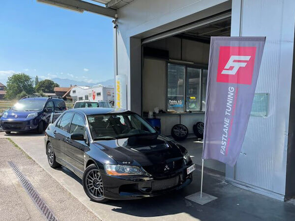 Ein schwarzer Mitsubishi Lancer Evolution 9 steht neben der Fastlane Tuning Schweiz Flagge