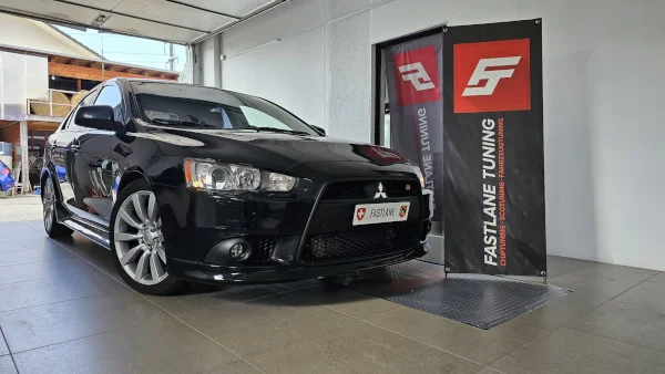 Ein schwarzer Mitsubishi Lancer steht neben dem Banner der Fastlane Tuning Schweiz GmbH