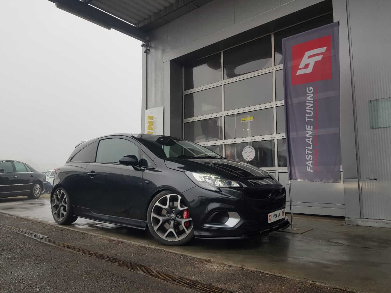 Ein schwarzer Opel Corsa OPC steht neben der Fastlane Tuning Schweiz Flagge