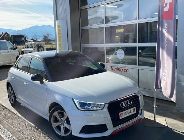 Ein weisser Audi A1 1.8 TFSI steht neben der Fastlane Tuning Schweiz Flagge.