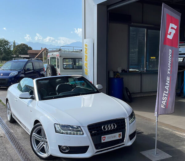 Ein weisses Audi A5 Cabrio steht neben der Fastlane Tuning Schweiz Flagge.