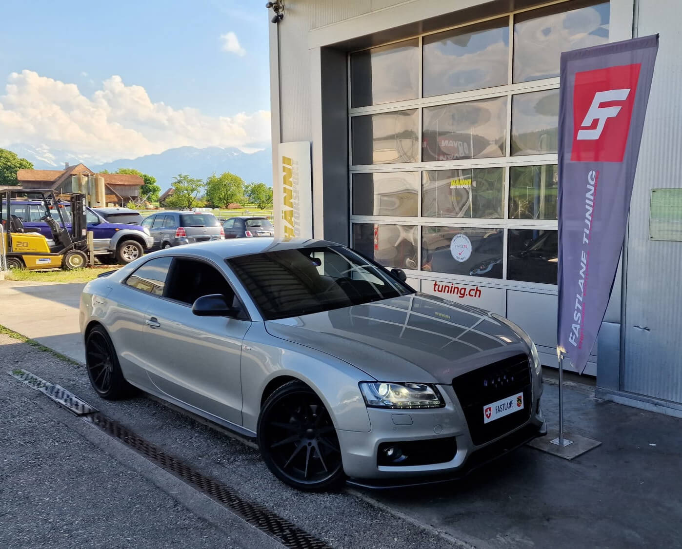 Ein grey Audi A5 steht neben das Fastlane Tuning Schweiz Flagge