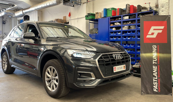 Ein kohlegrauer Audi Q5 2.0 TDI steht neben dem Banner der Fastlane Tuning Schweiz GmbH.