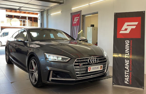 Ein kohlegrauer Audi S5 Sportback steht neben dem Banner der Fastlane Tuning Schweiz GmbH