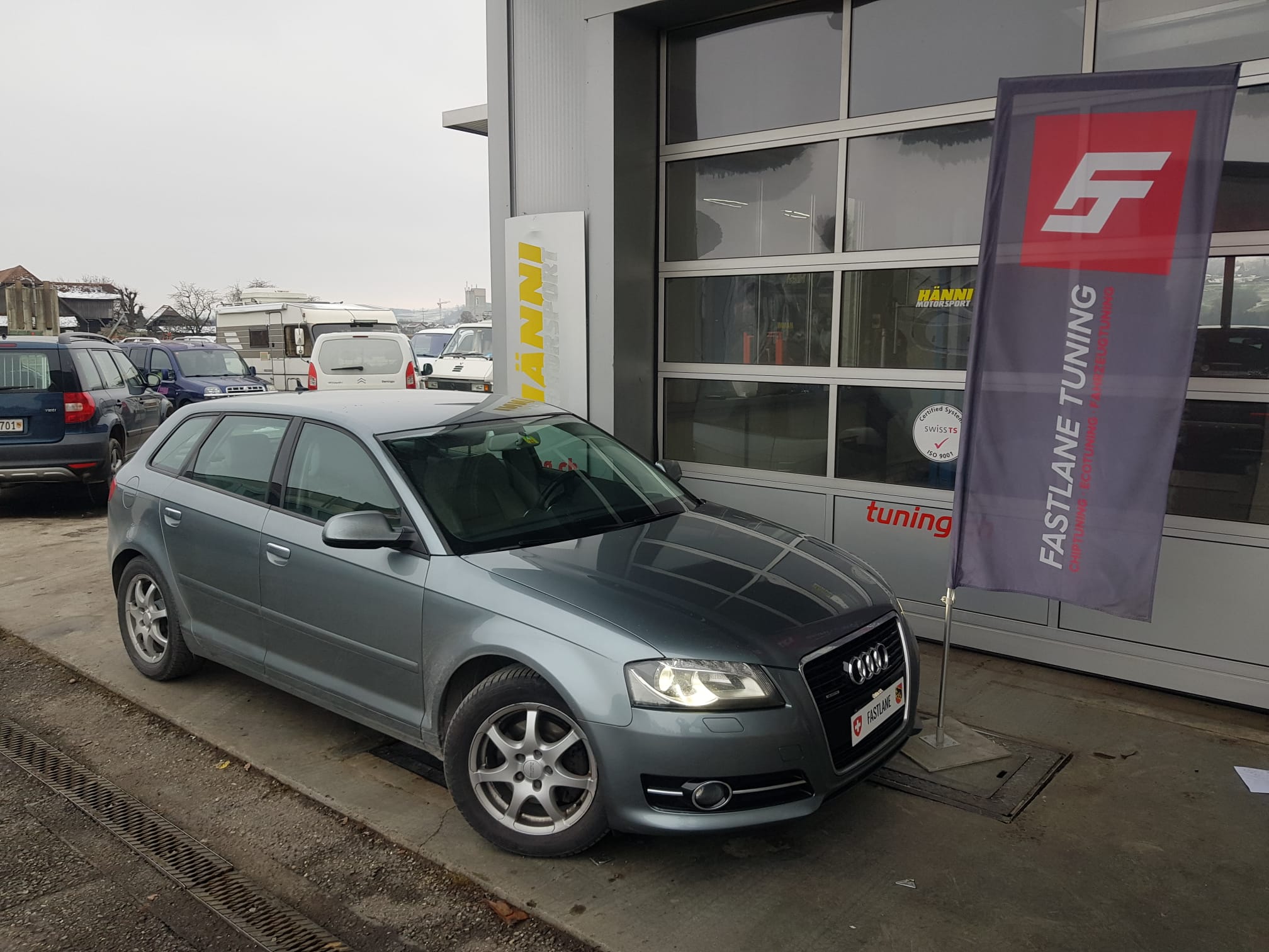 Ein grauer Audi A3 steht neben der Fastlane Tuning Schweiz Flagge