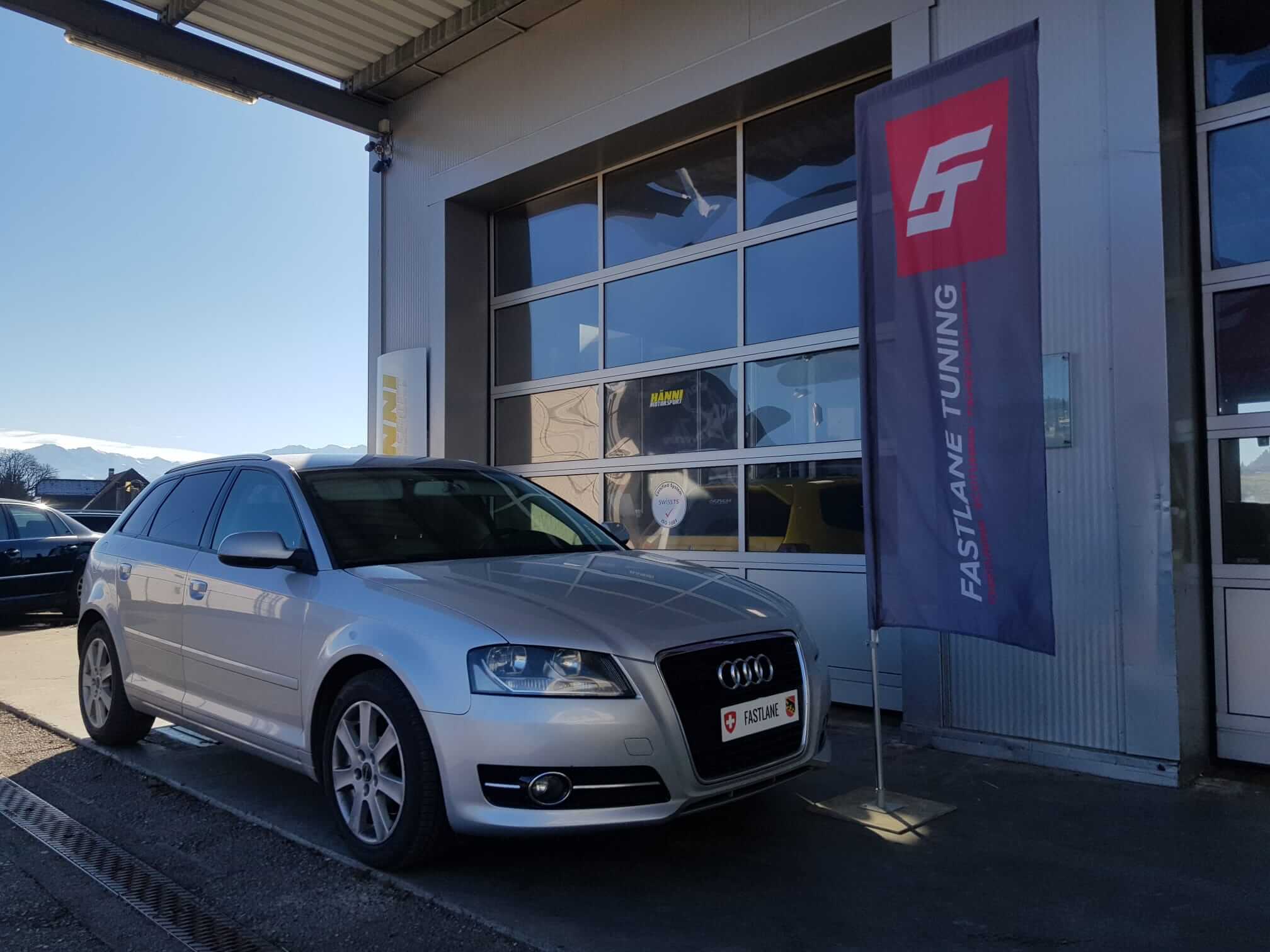 Ein grauen Audi A3 steht neben der Fastlane Tuning Schweiz flagge