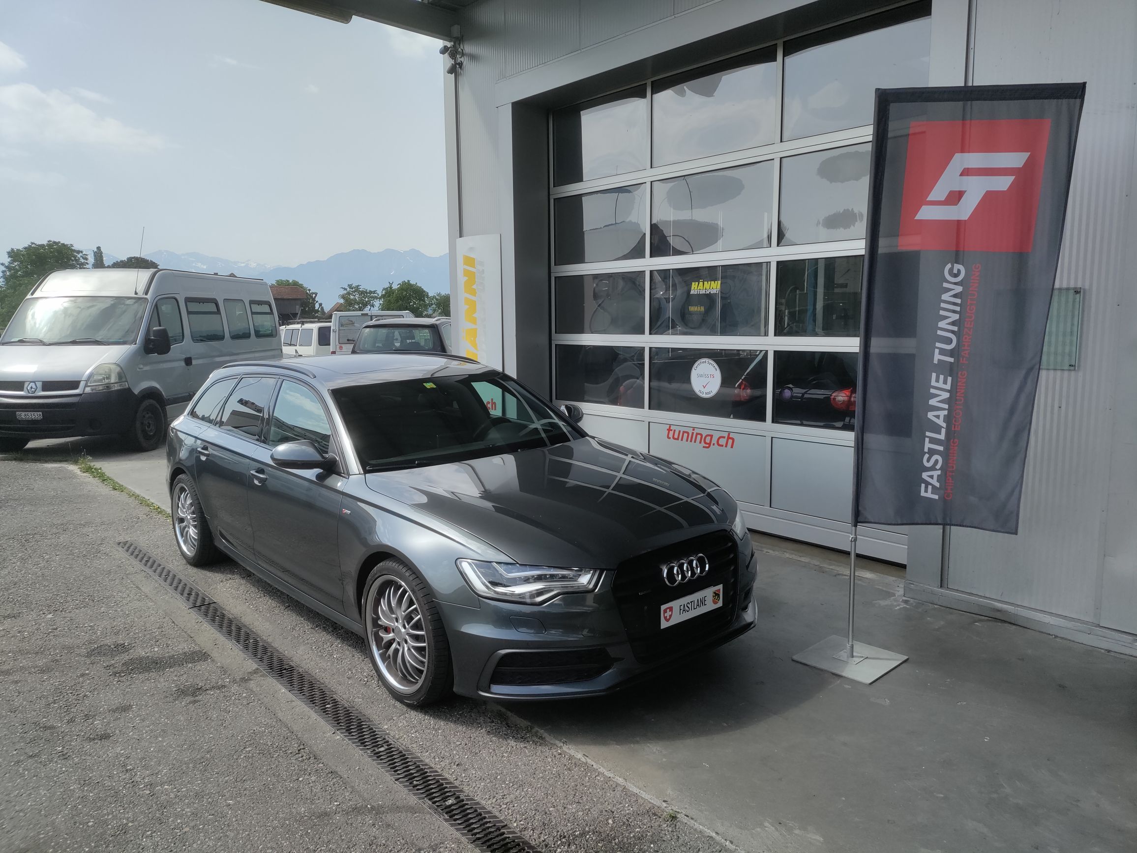 Ein anthrazitfarbener Audi A6 V6 TDI competition Kombi vor der Garage neben der Fastlane Tuning Schweiz Flagge