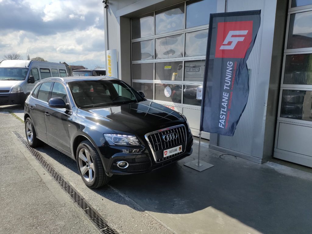 Ein schwarzer Audi Q3 2.0 TDI vor der Garage neben der Fastlane Tuning Schweiz Flagge