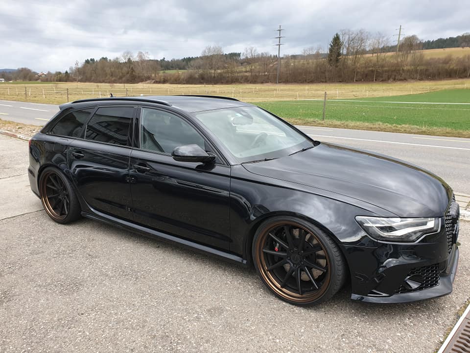 Ein schwarzer RS6 V8 mit braunen Sonderrädern und Frontschürze parkt auf der Straße in der Nähe der Garage