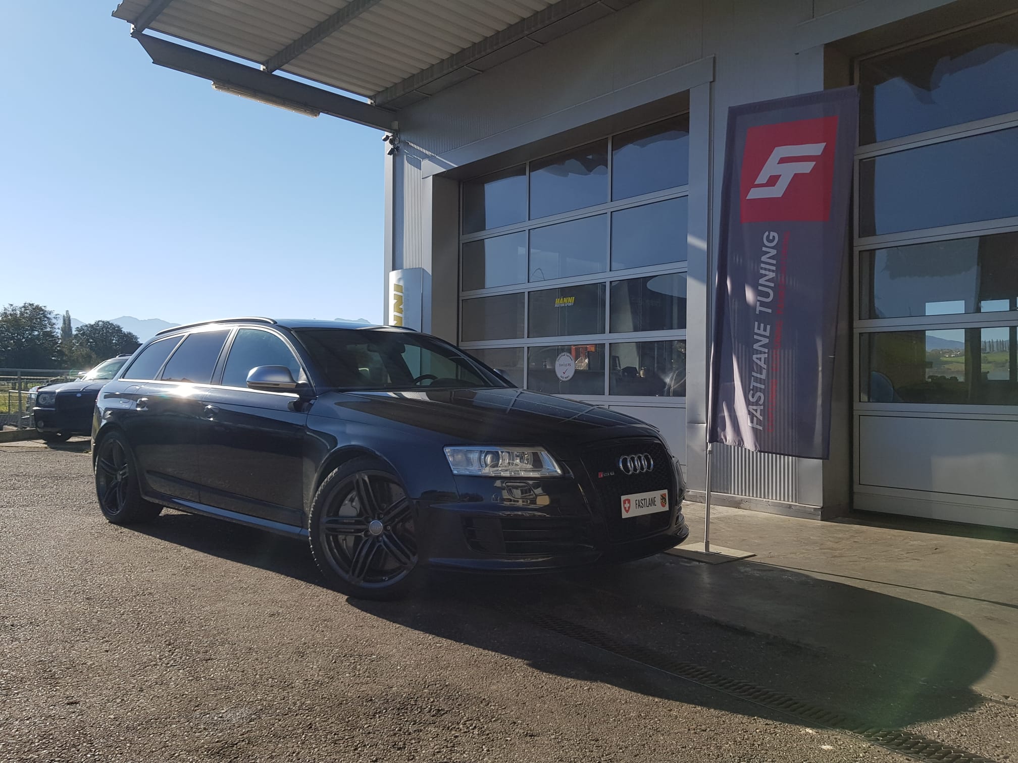 Ein schwarzer Audi RS6 V10 Biturbo steht neben der fastlane tuning shweiz Flagge