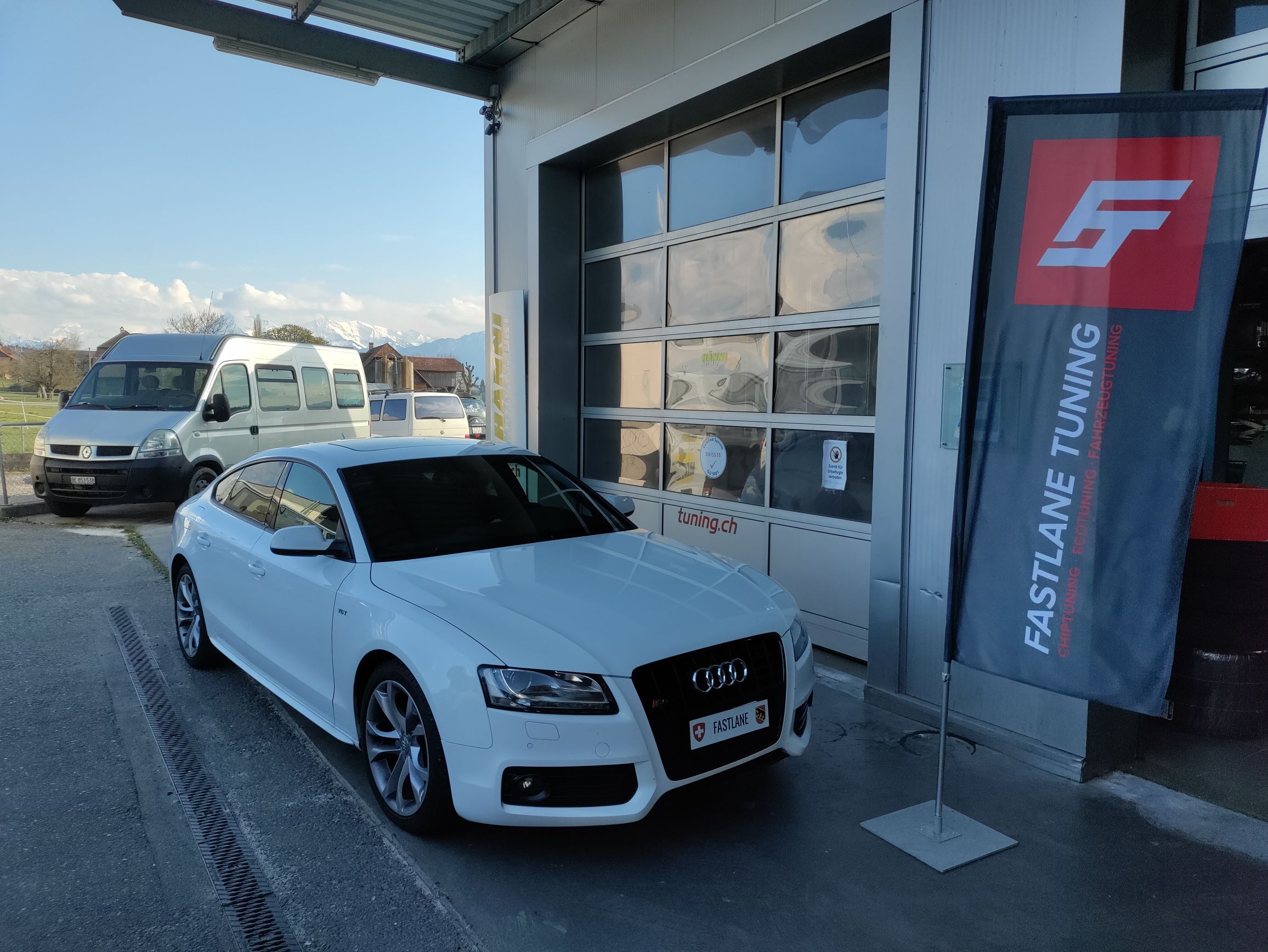 Ein weisser Audi S5 V6 kompressor steht vor der Garage neben der Fastlane Tuning Schweiz Flagge