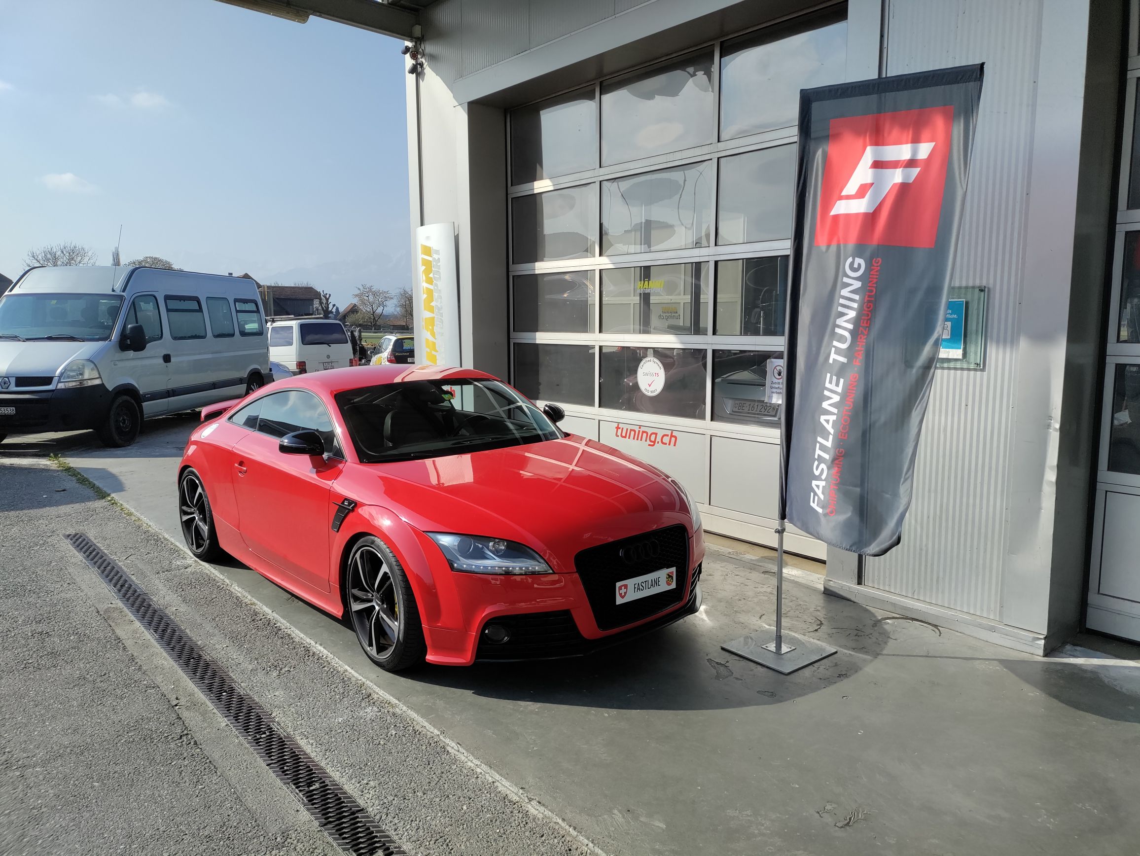 Audi TTS Mk2 Coupe Leistungstuning  Ein leuchtend roter Audi TTS Mark 2 Coupe parkt vor der Garage neben der Fastlane Tuning Schweiz-Flagge.