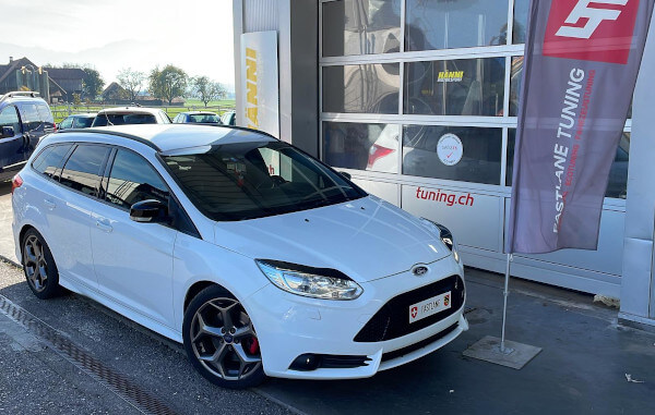 Ein weisser Ford Focus ST Mk3 Kombi steht neben der Fastlane Tuning Schweiz Flagge.