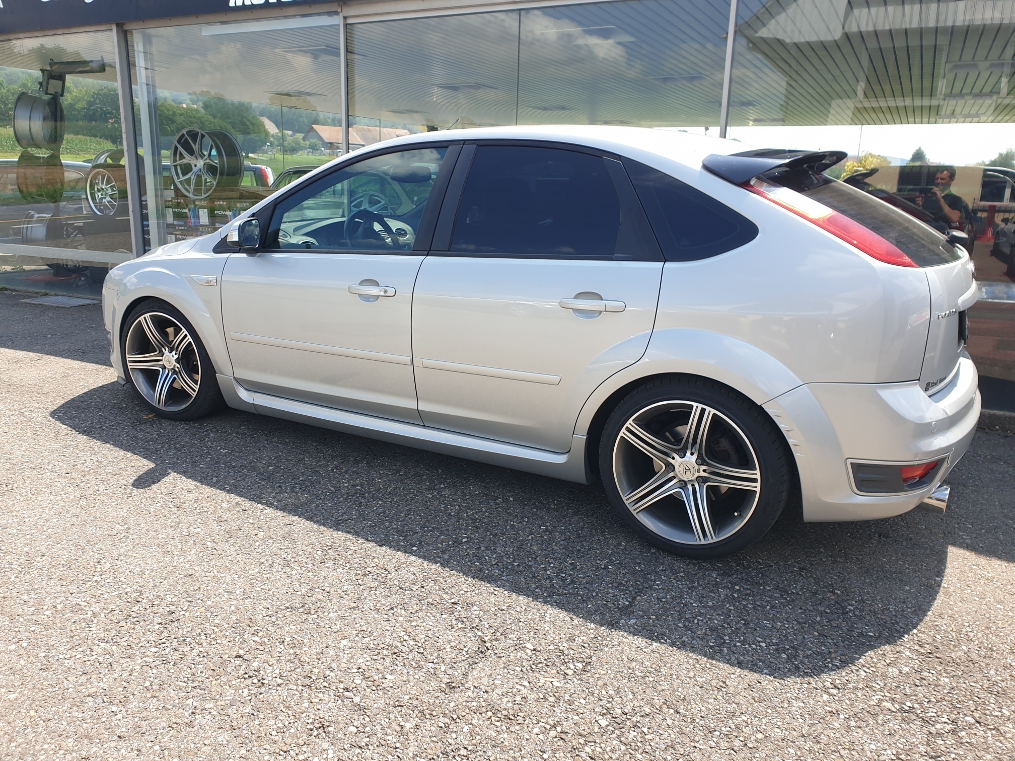 Ein silberner Ford Focus ST 225 mit Stage-2-Tuning steht vor der Garage neben der Fahrzeugausstellung