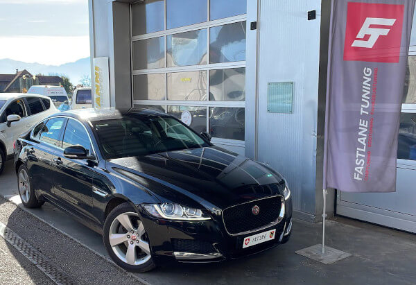 Ein schwarze Jaguar XF 2.2 D steht neben das Fastlane Tuning Schweiz GmbH flagge