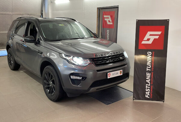 Ein kohlegrauer Landrover Discovery Sport 5 steht neben dem Banner der Fastlane Tuning Schweiz GmbH