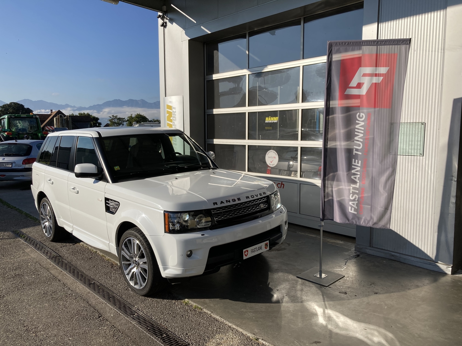 Ein weisser Landrover Discovery 4 HSE, der vor der Garage neben der Fastlane Tuning Schweiz Flagge geparkt ist.