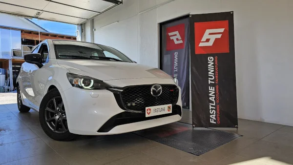 Ein weißer Mazda 2 steht neben dem Banner der Fastlane Tuning Shweiz GmbH