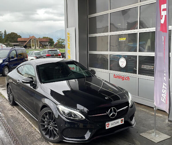 Ein schwarzes Mercedes C43 AMG Coupe steht neben der Fastlane Tuning Schweiz Flagge.