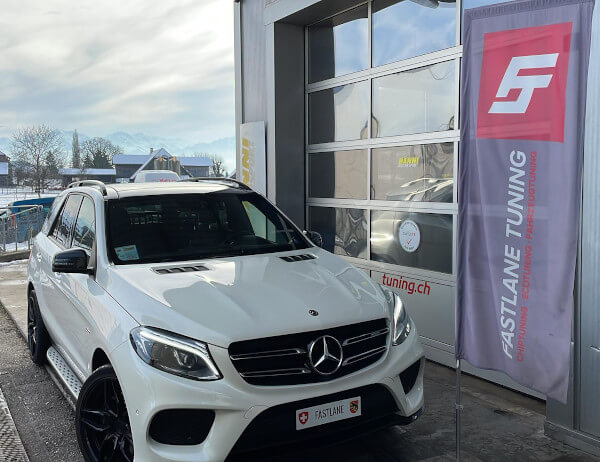 Ein weisser Mercedes Benz GLE 43 AMG steht neben der Fastlane Tuning Schweiz Flagge