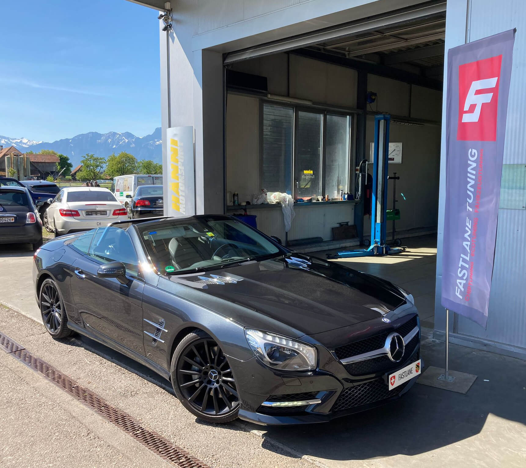 Ein anthrazitfarbenes Mercedes SL 500 Cabrio steht neben der Fastlane Tuning Schweiz Flagge.