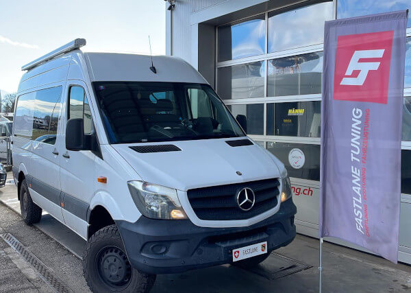 Ein weißer Mercedes Sprinter 4X4 Wohnmobil steht neben der Fastlane Tuning Schweiz Flagge