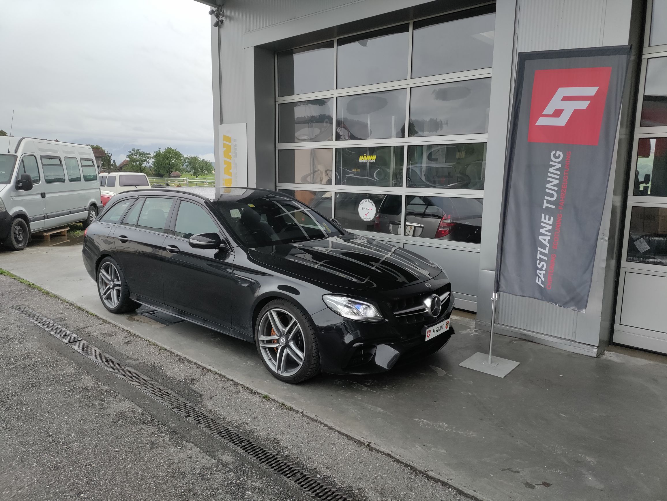 Ein Mercedes Benz E63 AMG S 2021 Facelift Kombi steht vor der Garage neben der Fastlane Tuning Schweiz Flagge