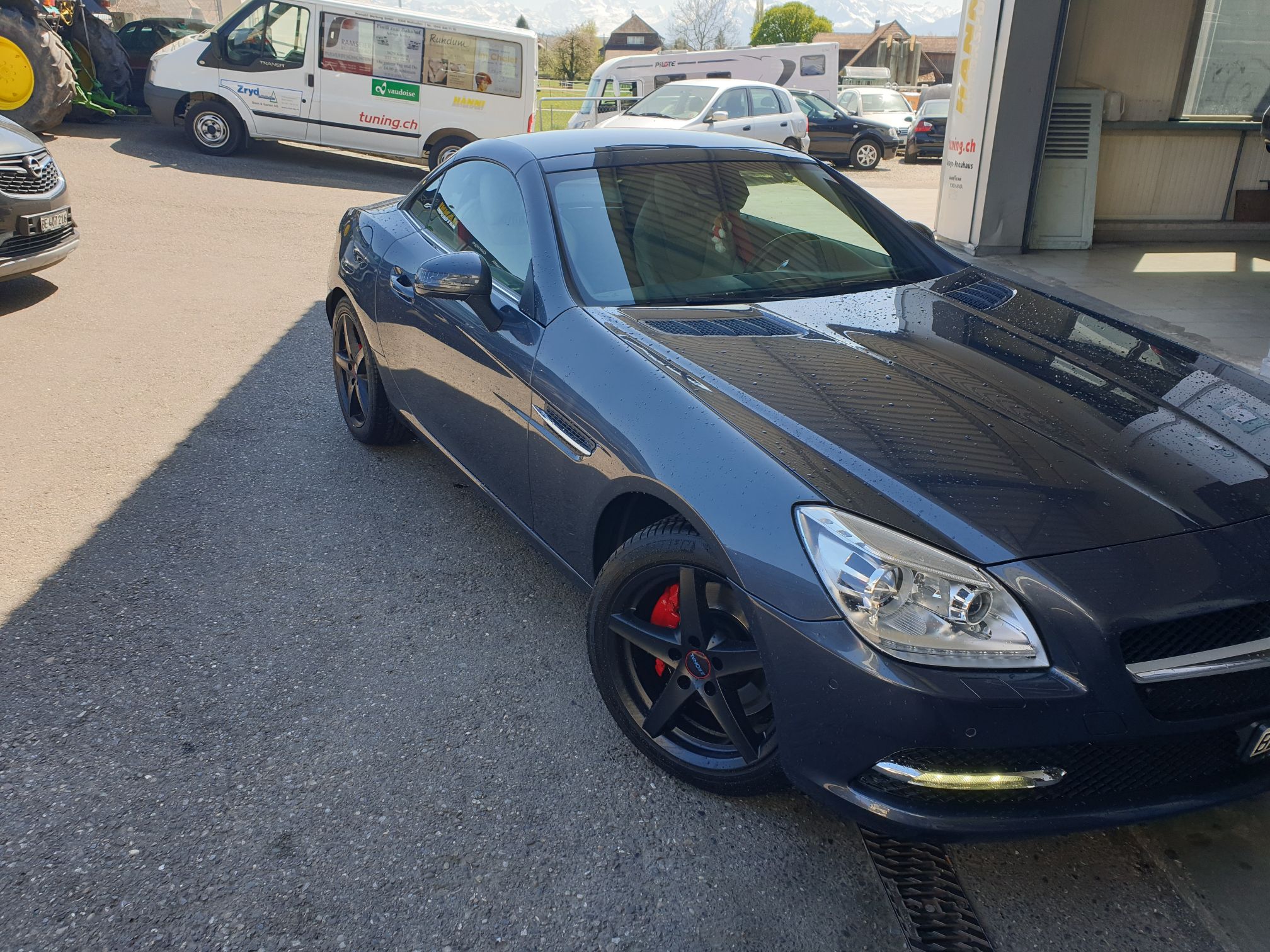 Ein grauer Mercedes Benz SLK 200 parkt vor der Garage neben der Fastlane Tuning Schweiz Flagge