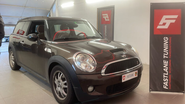 Ein brauner Mini Clubman Cooper S steht neben dem Banner der Fastlane Tuning Schweiz GmbH