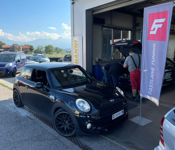 Ein schwarzer Mini Cooper S 2.0 F56 steht neben der Fastlane Tuning Schweiz Flagge