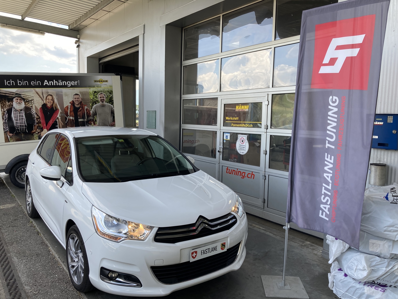 Ein weisser Citroen C4 Diesel vor der Garage neben der Fastlane Tuning Schweiz Flagge