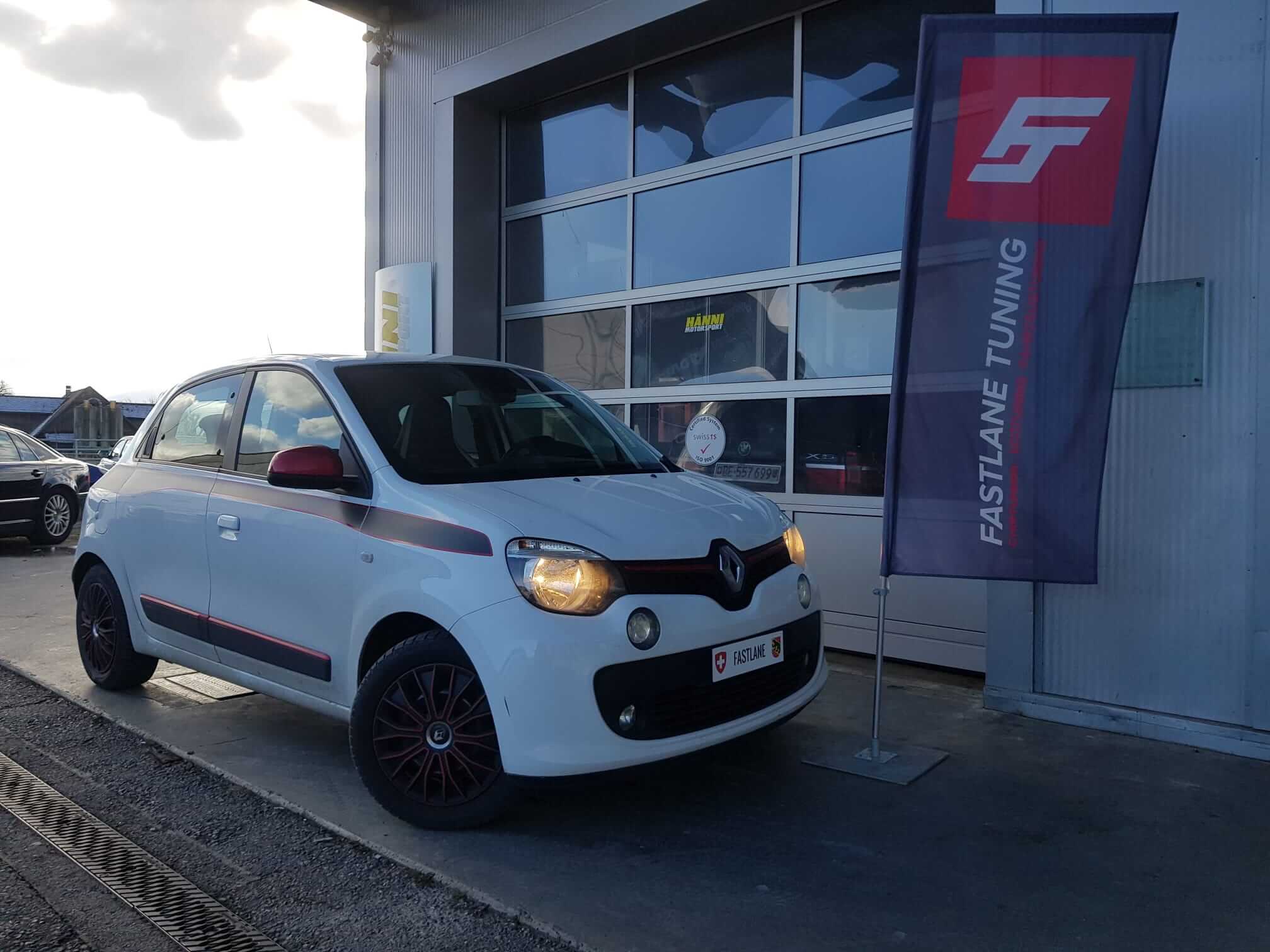 Ein weiss Renault Twingo TCe 90 steht neben den Fastlane Tuning Schweiz flagge