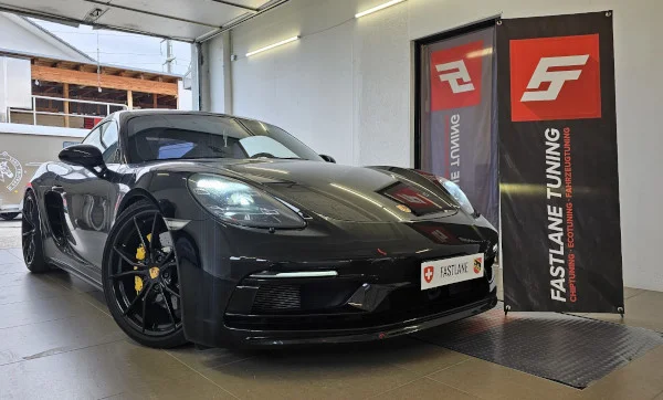 Neben dem Banner von Fastlane Tuning Schweiz steht ein schwarzer Porsche Cayman GTS.