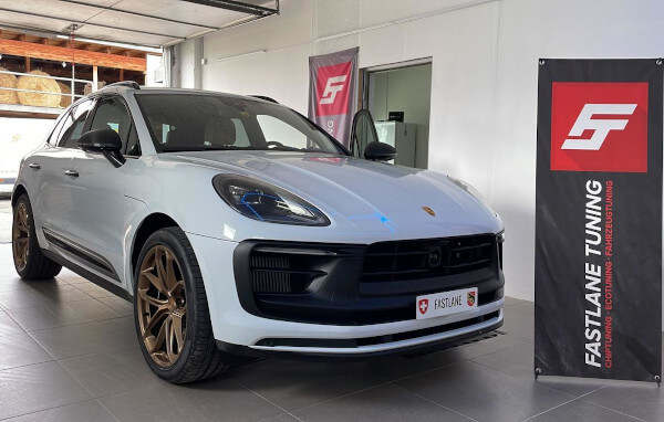 Ein weisser Porsche Macan GTS V6 steht neben dem Banner der Fastlane Tuning Schweiz GmbH.