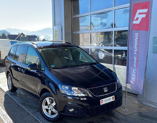 Ein schwarzer SEAT Alhambra 2.0 TDI steht neben der Fastlane Tuning Schweiz Flagge.