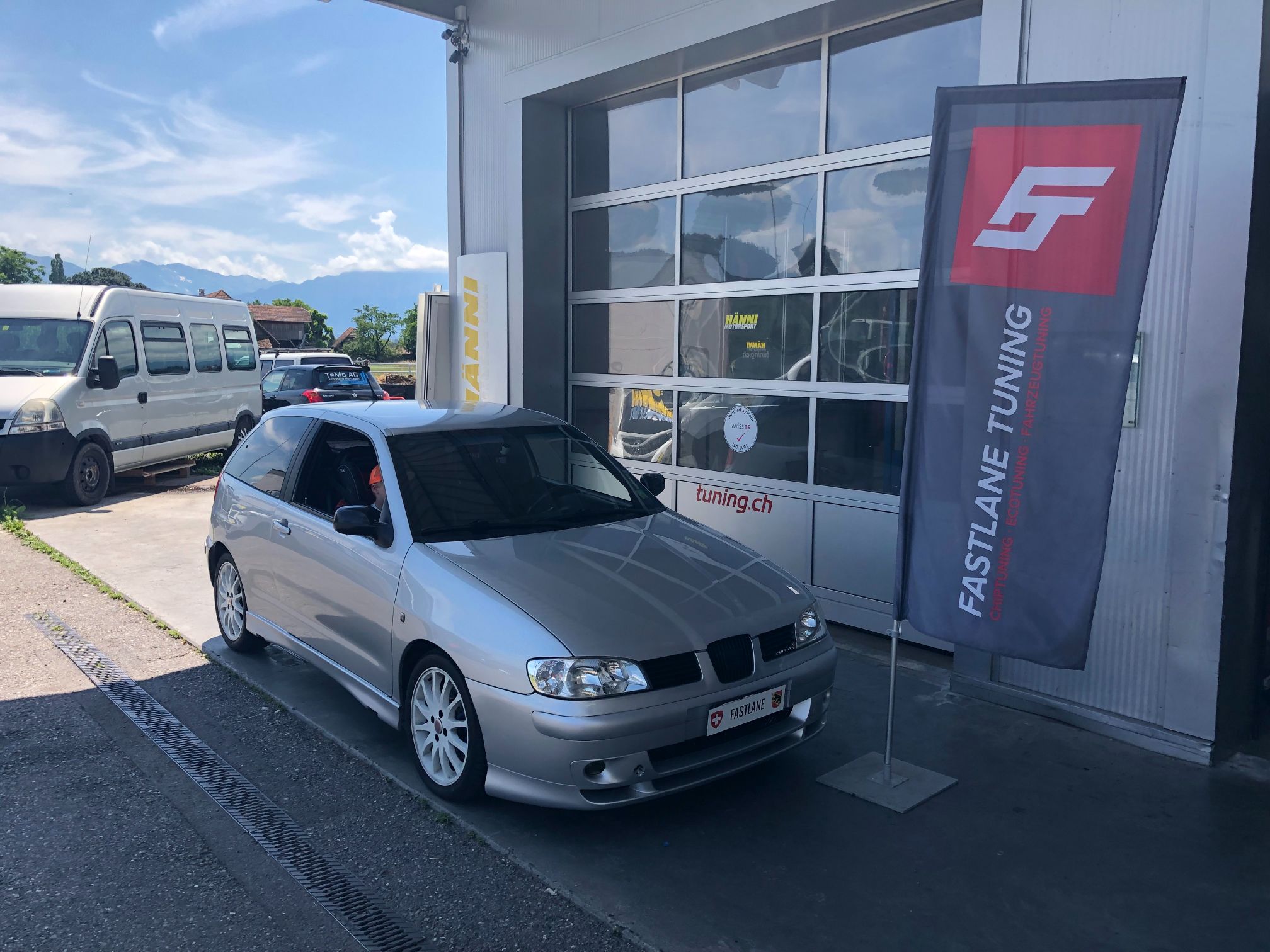 Ein silberner SEAT Ibiza steht vor der Garage neben der Fastlane Tuning Schweiz Flagge