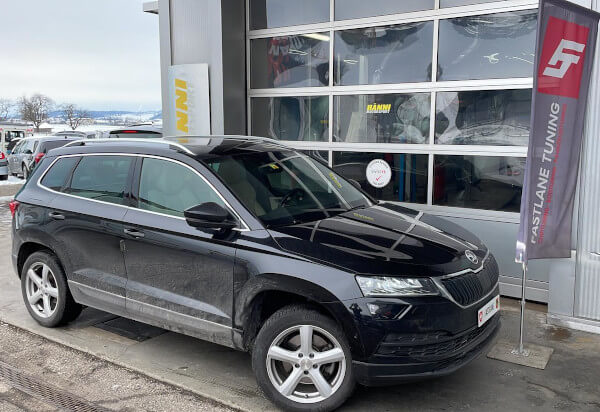 Ein Schwarze Skoda Karoq steht neben das Fastlane Tuning Schweiz flagge.