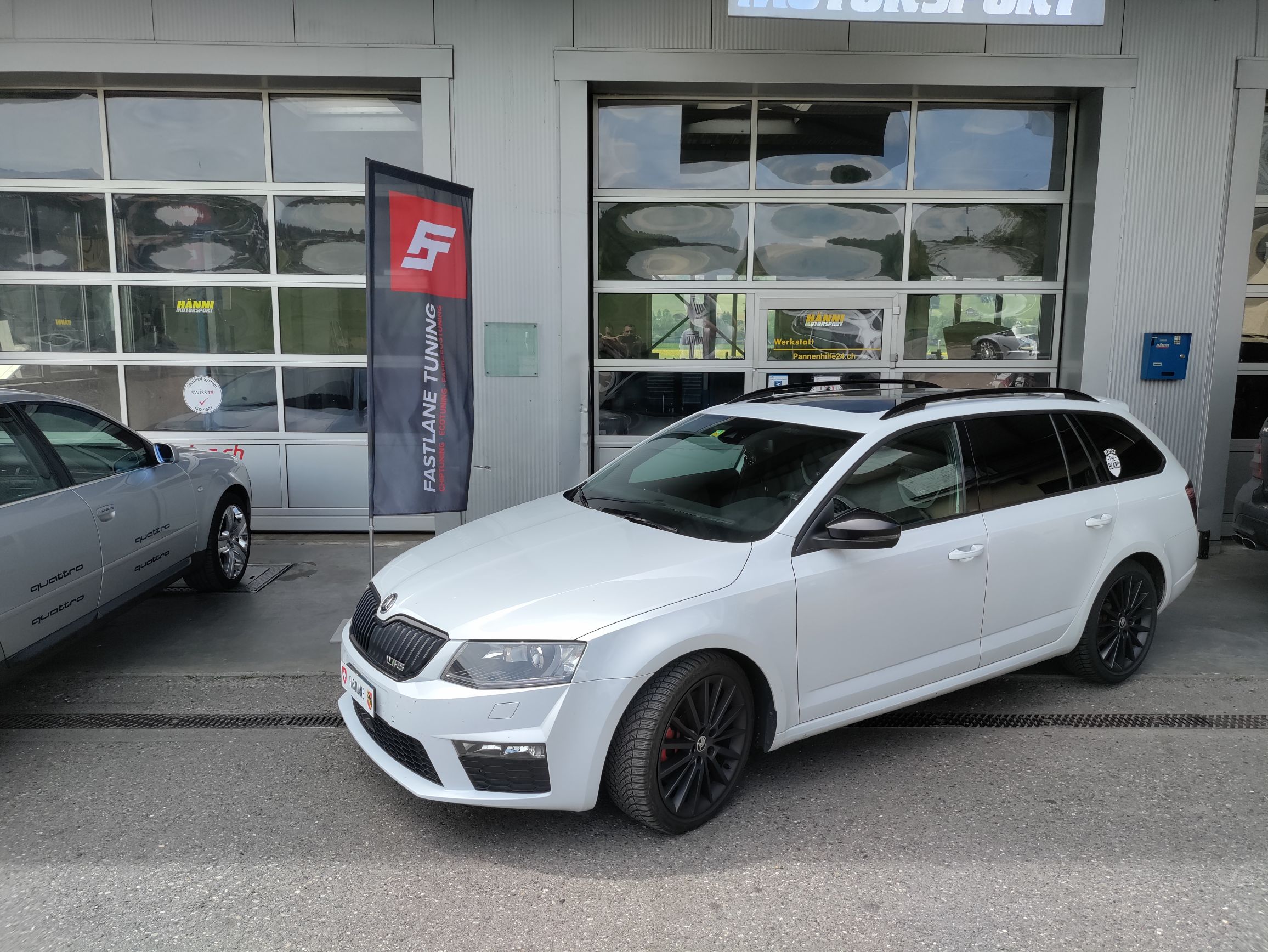 Ein weisser Skoda Octavia steht neben der Fastlane Tuning Schweiz Flagge