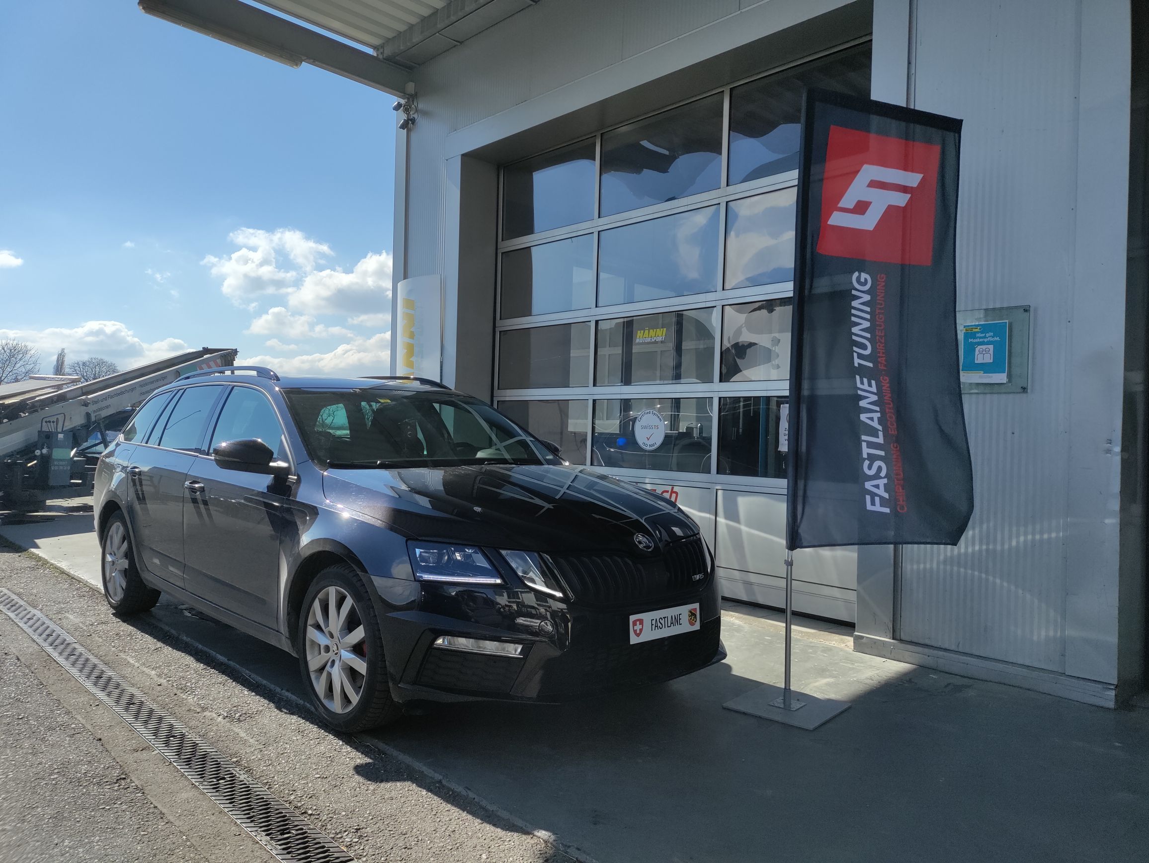 Ein schwarzer Skoda Octavia IV RS steht vor der Garage neben der Fastlane Tuning Schweiz Flagge