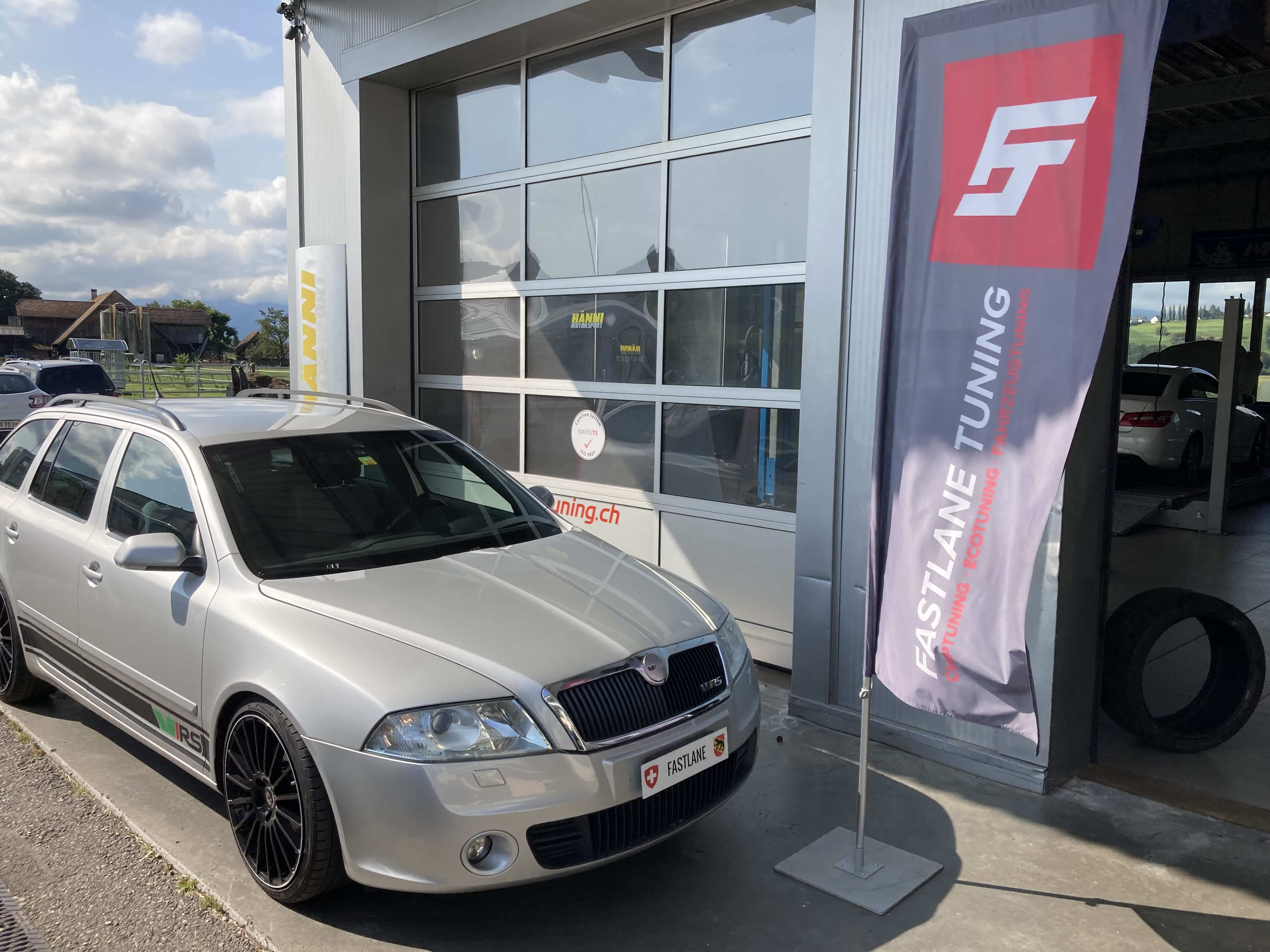 Ein silberner Skoda Octavia II RS steht vor der Garage neben der Fastlane Tuning Schweiz Flagge