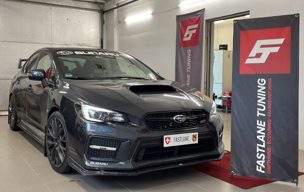 Ein kohlegrauer Subaru Impreza WRX STI steht neben dem Banner der Fastlane Tuning Schweiz GmbH