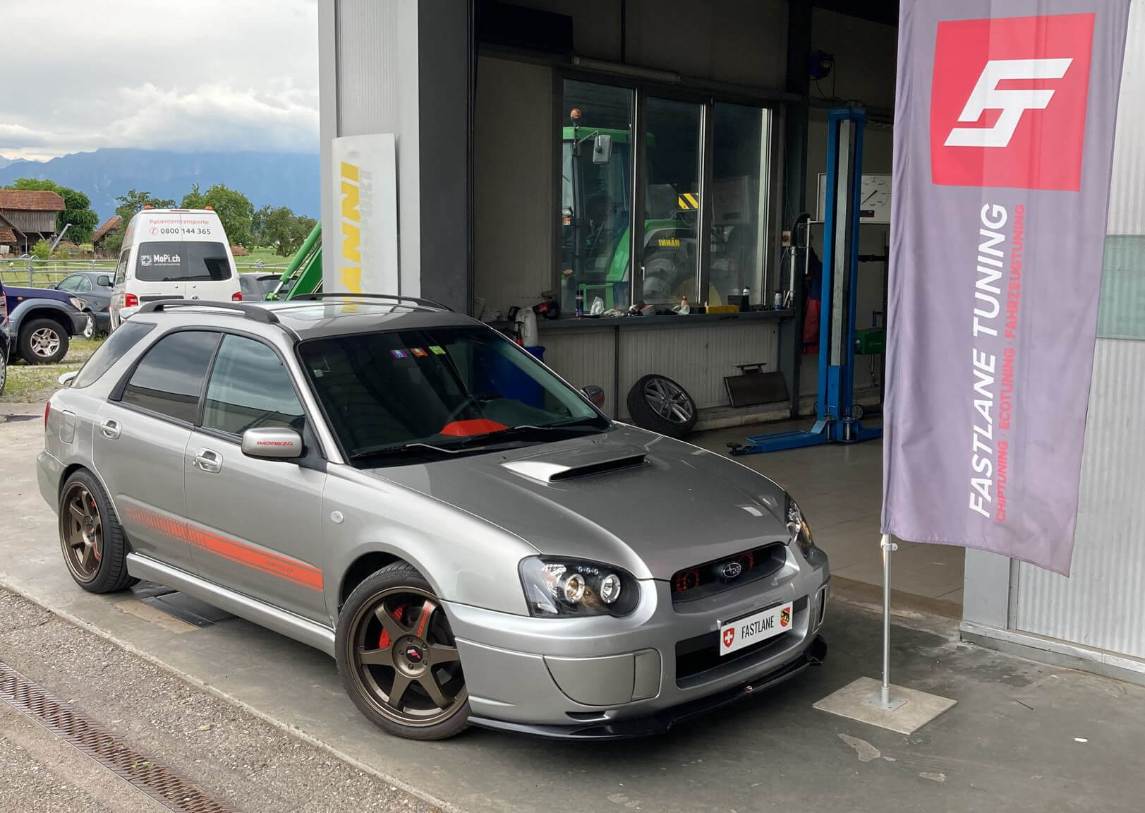 Ein grauer Subaru Impreza WRX 2003 steht neben der Fastlane Tuning Schweiz Flagge.