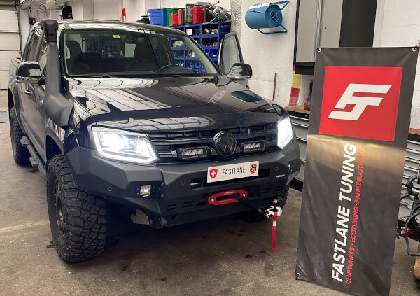 Ein schwarzer Monster 4WD VW Amarok steht neben dem Banner von Fastlane Tuning Schweiz