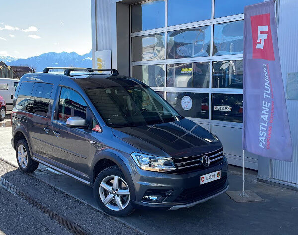 Ein grauer Volkswagen Caddy 2.0 TDI steht neben der Fahne der Fastlane Tuning Schweiz GmbH