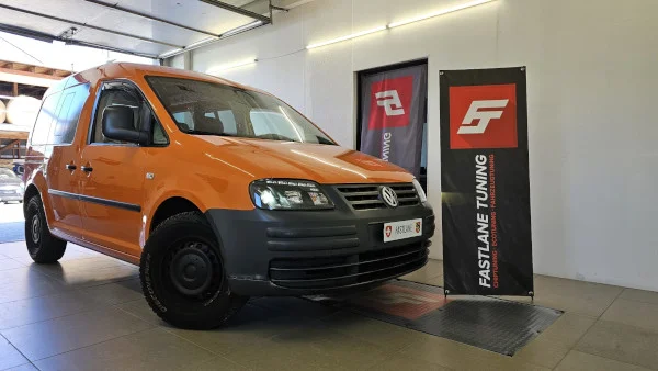 Ein orangefarbener Volkswagen Caddy mit schwarzen Felgen steht neben dem Banner der Fastlane Tuning Schweiz GmbH