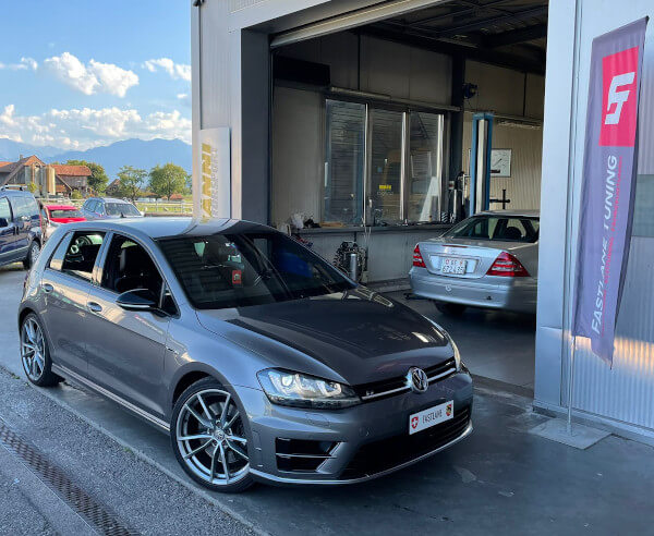 Ein grauer VW Golf 7R steht neben der Fastlane Tuning Schweiz Flagge. Er wurde speziell so modifiziert, dass er beim Verzögern ein leichtes Knurren von sich gibt.