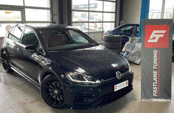 Ein schwarzer Golf 7 R steht neben dem Banner von Fastlane Tuning Schweiz