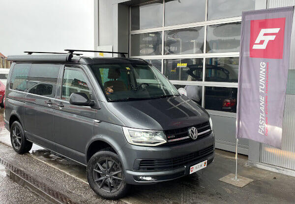 Ein grauer VW T6 California 4WD Wohnmobil steht neben der Fastlane Tuning Schweiz Flagge